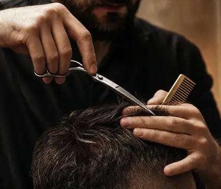 Le forbici che tagliano una ciocca sopra la testa di un cliente, con il pettine pronto