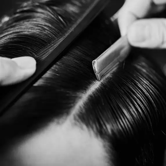 Un rasoio e un pettine aprono la riga su capelli scuri pettinati all’indietro