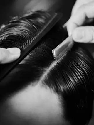 Un rasoio e un pettine aprono la riga su capelli scuri pettinati all’indietro