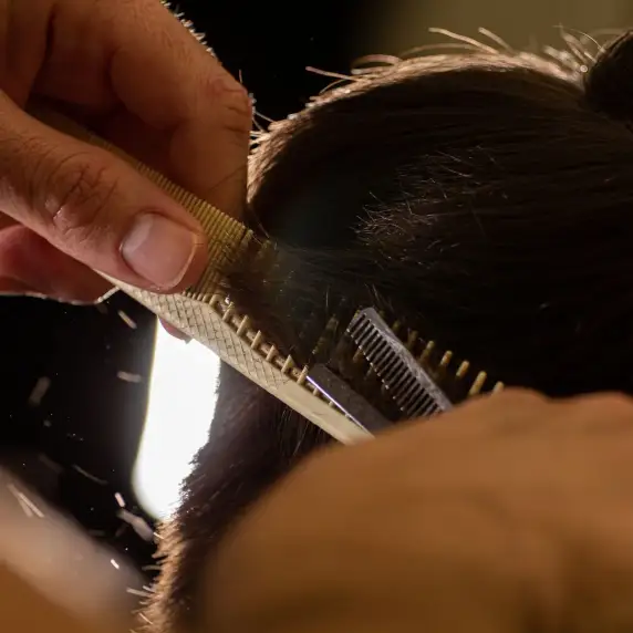 Un pettine solleva una ciocca di capelli e le forbici tagliano appena sotto