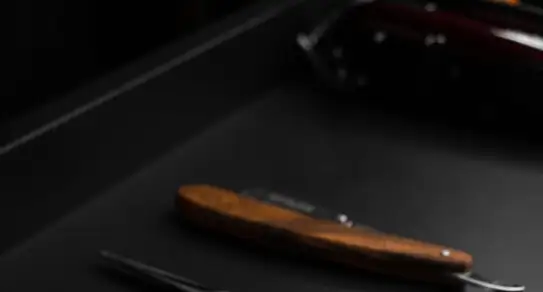 Un rasoio a mano libera con il manico in legno, posato sul piano nero